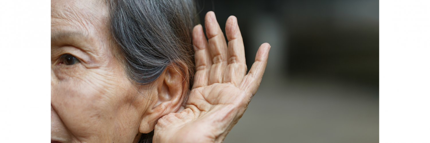 Older woman holding one hand up and cupping it around her ear, trying to hear.